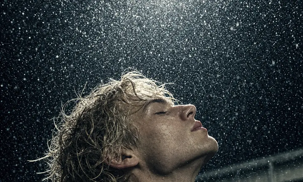 SS26 lookbook, Obsession: a man in a dark coat looking up into falling rain at night